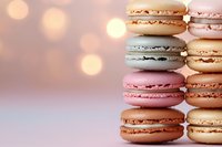 Colorful French macarons stacked in rows against soft pink bokeh background, featuring pastel shades of pink, beige, and gray. Sweet dessert photography.