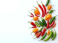 Assorted hot chili peppers in red, orange, and green varieties arranged on white background. Fresh spicy ingredients for cooking and culinary design.