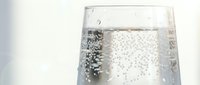 Close-up of sparkling water glass with effervescent bubbles rising to surface against clean white background for refreshment and hydration concepts.