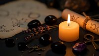 Mystical fortune telling setup with burning candle, black stones, dried herbs and ancient scrolls creating atmospheric divination scene for spiritual practices.