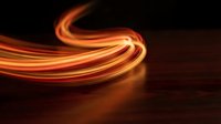 Glowing orange and yellow light trails curve dynamically across dark background, creating abstract motion effect suitable for technology, energy, and modern design projects.