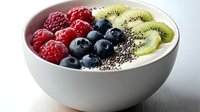 Fresh yogurt bowl topped with raspberries, blueberries, sliced kiwi and chia seeds arranged in colorful rows against white ceramic background for healthy breakfast.