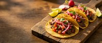 Mexican street tacos with seasoned beef, fresh cilantro, onions, and lime wedges served on wooden board for restaurant menus and food blogs.