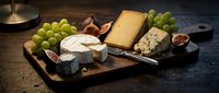 Assorted cheeses with green grapes, figs, and knife on wooden board, gourmet charcuterie spread for entertaining and food styling.