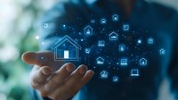 Digital smart home automation concept with glowing house and device icons floating above open palm against blurred background, illustrating IoT technology.