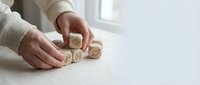 Hands arranging wooden dice with question marks on white surface, representing uncertainty, decision making and problem solving in business strategy.