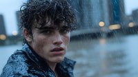 Young Hispanic male model with wet curly hair in heavy rain, dramatic moody portrait showing intense emotional expression against blurred urban background with bokeh lights.