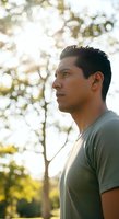 Young man of Latin American descent in casual gray t-shirt gazing thoughtfully outdoors among trees during golden hour, suitable for lifestyle and wellness content.
