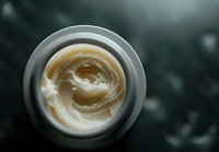 Overhead view of creamy moisturizer swirled in white container against dark background, showing luxurious texture and natural skincare product consistency.