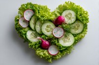 Fresh heart-shaped salad with cucumber slices, radishes and lettuce leaves on white background for healthy eating and diet concept.