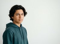 Young man with dark wavy hair and olive complexion wearing teal hoodie, looking over shoulder against white background for portrait and lifestyle use.