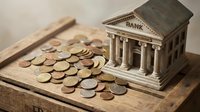 Miniature bank building model with scattered coins on wooden tray representing financial savings, investment planning, and money management concepts.