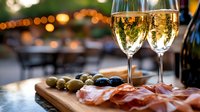 Elegant champagne flutes with sparkling wine alongside charcuterie board with prosciutto, olives and appetizers against blurred bokeh lights background for fine dining.
