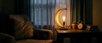 Cozy living room interior with warm crescent moon table lamp glowing softly beside comfortable sofa creating intimate atmospheric lighting for home decor.