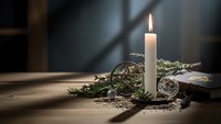Burning white candle with evergreen branches and decorative spheres on wooden surface creating cozy winter holiday atmosphere for seasonal decor.