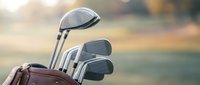 Golf clubs in leather bag with warm sunlight creating bokeh background for sports and recreation themes.