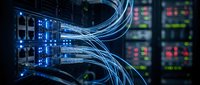 Fiber optic cables with blue light connected to server equipment in data center, representing network infrastructure and telecommunications technology.