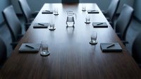 Empty conference table with place settings, water glasses, and chairs arranged for business meeting or corporate event planning.