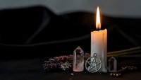 Burning white candle with pentagram pendant and crystals creating mystical witchcraft altar setup for spiritual rituals and meditation practices.