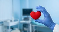 Medical professional in blue gloves holding red heart symbol in modern hospital setting representing healthcare, cardiology and patient care.