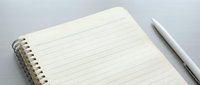 Open spiral notebook with lined pages and white pen on gray surface for writing notes and planning tasks.
