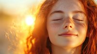 Young redhead woman with freckles enjoying warm sunlight with closed eyes and peaceful smile, golden hour portrait capturing serenity and natural beauty in soft focus.