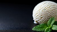 Creamy vanilla ice cream scoop with fresh mint leaves on dark background, textured frozen dessert close-up with copy space for menu or advertising.