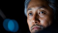 Mature Asian businessman with gray hair looking thoughtfully upward in dramatic lighting, conveying wisdom and contemplation in corporate environment.