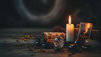 Mystical fortune telling setup with burning candle, tarot cards, crystal ball and dried herbs on dark wooden surface for spiritual divination practices.