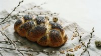 Fresh baked challah bread with poppy seeds on linen cloth with pussy willow branches for Easter and spring celebration table setting.