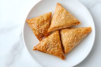 Golden crispy phyllo pastry triangles with sesame seeds served on white plate against marble background. Middle Eastern appetizer for restaurant menu.