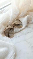 Elegant gold aviator sunglasses resting on soft white fabric against marble surface creating luxurious fashion accessory flatlay composition.