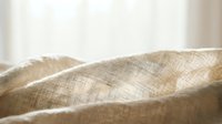 Natural linen fabric texture with soft folds and gentle lighting creating warm beige tones for textile and interior design projects.