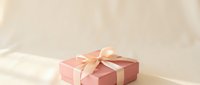 Close-up of a pink gift box with a gold ribbon bow on a neutral beige background, suitable for holiday, celebration, and greeting card designs.
