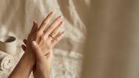 Female hands with natural manicure applying moisturizer cream in soft morning light. Skincare routine, beauty treatment, hand care concept.