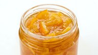 Homemade apricot jam in glass jar with preserved fruit pieces and golden syrup, ready for culinary use.