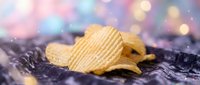 Golden crispy potato chips scattered on dark textured surface with colorful bokeh lights creating festive party atmosphere for snack food advertising.