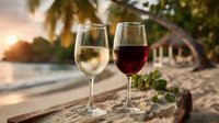 Two wine glasses with white and red wine on wooden surface at tropical beach sunset with palm trees and ocean view for romantic vacation dining.