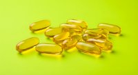 Golden vitamin capsules scattered on bright green background for health and wellness supplement advertising.