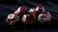 Raw red garnet gemstones cluster on dark textured surface showcasing natural mineral crystal formation and deep burgundy coloration for jewelry making.