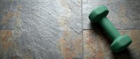 Green dumbbell on slate tile floor with natural stone texture, suitable for fitness, wellness, gym, and health-related design projects.