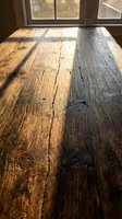 Wooden table surface with natural sunlight casting shadows through windows, showing grain texture and weathered finish for interior design and home decor projects.