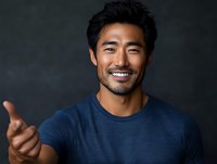 Confident Asian male professional in blue t-shirt showing positive gesture against dark background, displaying genuine smile and friendly expression.