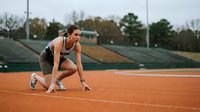 Female athlete in starting position on orange running track at outdoor stadium ready to sprint during training session.