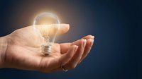 Glowing light bulb floating above open palm against dark background symbolizing innovation, creativity, and bright ideas for business solutions.