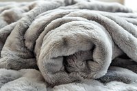 Soft plush gray blanket rolled up showing texture and layers of cozy faux fur material, close-up macro photography with selective focus for home decor and comfort.