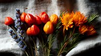 Fresh seasonal arrangement with vibrant orange physalis fruits, purple lavender stems and bright marigold flowers on textured linen background in moody lighting.