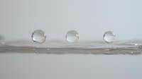 Clear water drops in line formation on reflective surface with soft gray background, showing surface tension and pure liquid properties. Macro photography captures nature.