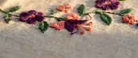 Delicate floral embroidery with burgundy and coral chrysanthemums on natural linen fabric showcasing traditional needlework craftsmanship and textile artistry.