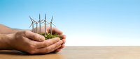 Hands holding miniature wind turbines with green grass against clear sky, representing renewable energy, sustainability, and environmental conservation for eco-friendly power generation concepts.